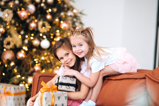 Dos niñas están jugando con regalos de año nuevo por el árbol en el sofá