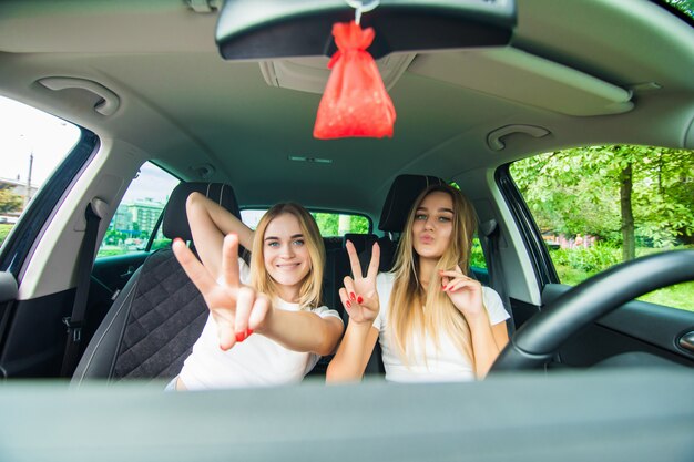 Dos niñas felices sentadas en el auto y gesticulando con el signo de la victoria se divierten mientras viajan