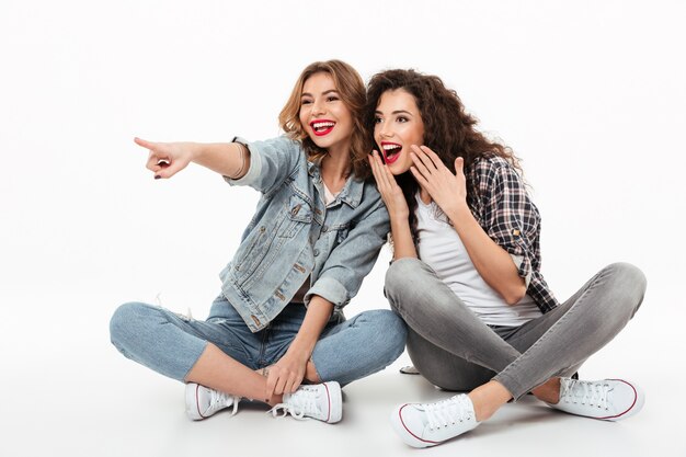 Dos niñas felices sentados juntos en el suelo y mirando a otro lado sobre la pared blanca