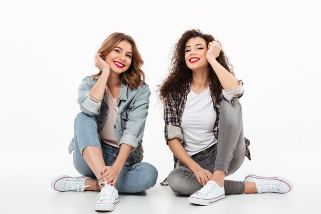 Dos niñas felices sentados juntos en el suelo sobre la pared blanca