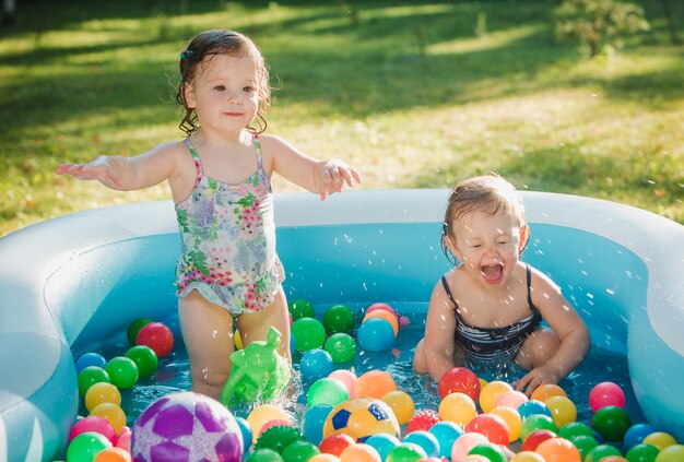 Las dos niñas jugando con juguetes en la piscina inflable en el día soleado de verano