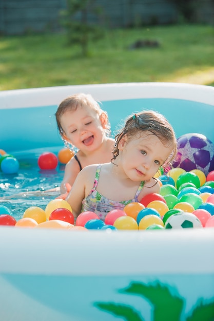 Las dos niñas jugando con juguetes en la piscina inflable en el día soleado de verano