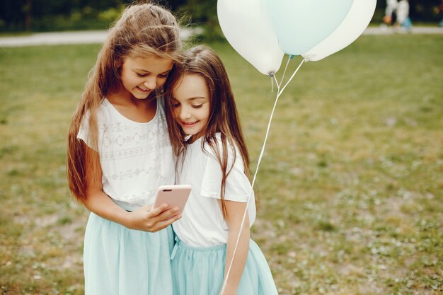 dos niñas lindas en camisetas blancas y faldas azules juegan en el parque de verano con globos