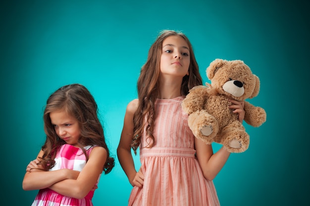 Foto gratuita las dos niñas lindas sobre fondo azul con osito de peluche