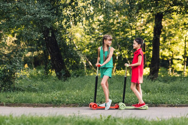 Dos niñas de pie en patinete scooter en el camino de campo