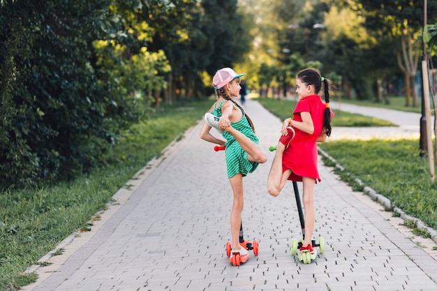 Foto gratuita dos niñas de pie sobre el patinete scooter estirando sus piernas