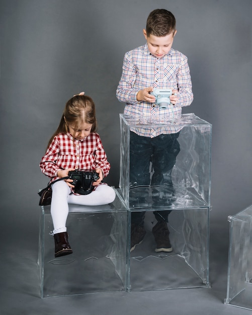 Foto gratuita dos niños con bloques transparentes mirando la cámara contra el fondo gris