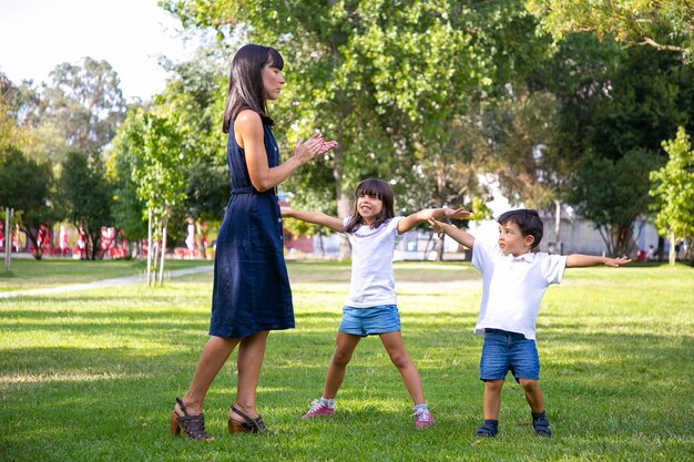 Dos niños lindos felices y su mamá jugando juegos activos al aire libre, haciendo ejercicios sobre el césped en el parque. Concepto de ocio y actividad familiar al aire libre