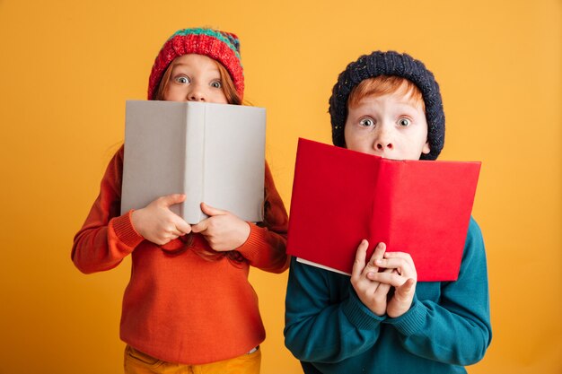 Dos niños pelirrojos asustados cubriéndose los rostros con libros.