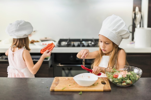 Dos niños pequeños en el sombrero del cocinero que prepara la comida en cocina