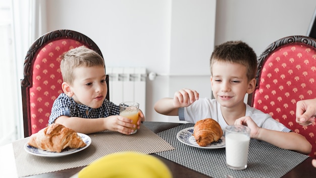 Foto gratuita dos niños sentados en una silla con un vaso de leche y croissants sobre el escritorio