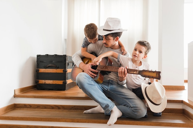 Dos niños sentados con su padre tocando la guitarra.