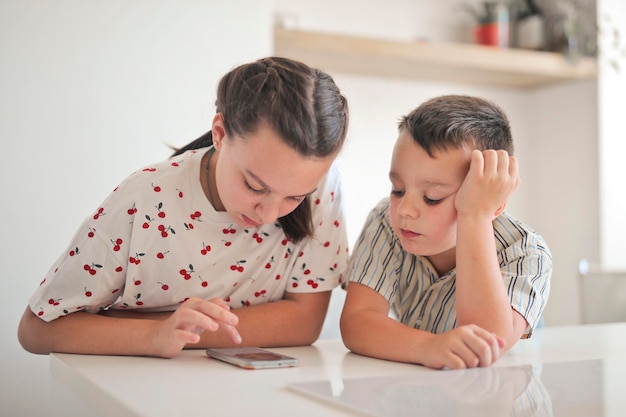 Dos niños usan un teléfono inteligente en la cocina.