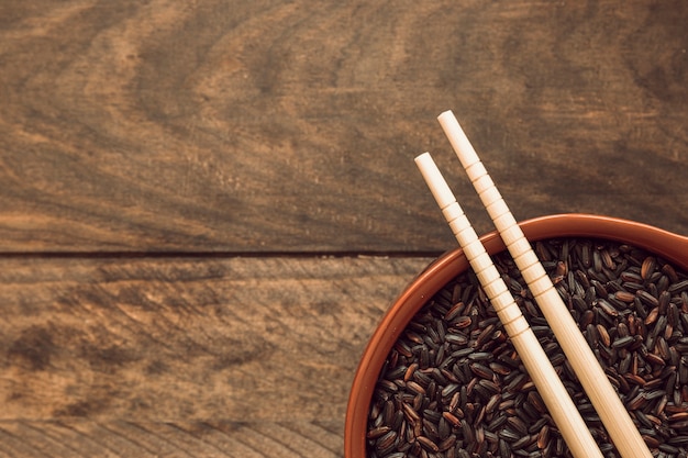 Dos palillos sobre el cuenco de grano de arroz negro sobre fondo de madera