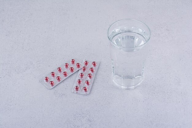 Dos paquetes de medicamentos rojos y un vaso de agua sobre la superficie de mármol. Foto de alta calidad