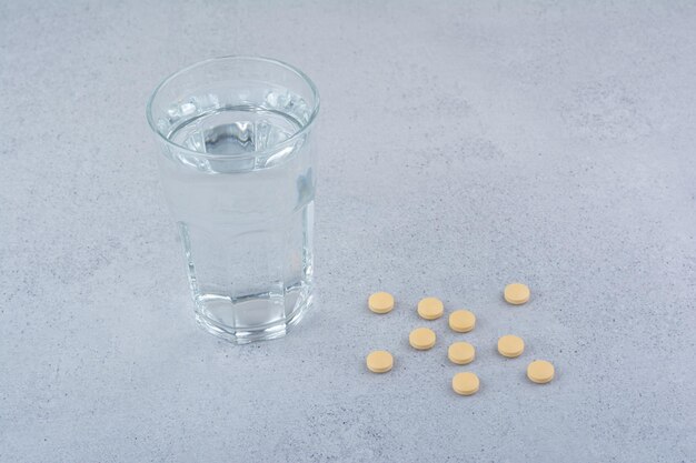 Dos paquetes de pastillas rojas con un vaso de agua.