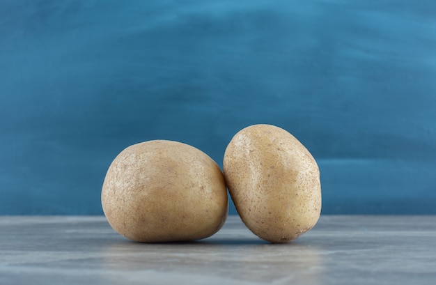 Dos patatas maduras, sobre la mesa de mármol.