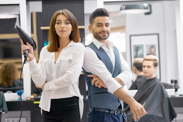 Dos peluqueros posando de pie en un moderno y espacioso salón de belleza