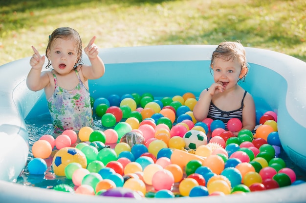 Las dos pequeñas niñas jugando con juguetes en la piscina inflable en el día soleado de verano