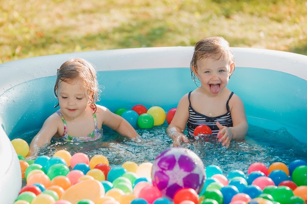 Las dos pequeñas niñas jugando con juguetes en la piscina inflable en el día soleado de verano