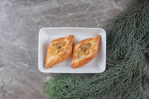 Dos pequeñas pides turcas en un plato junto a las ramas de pino en la superficie de mármol