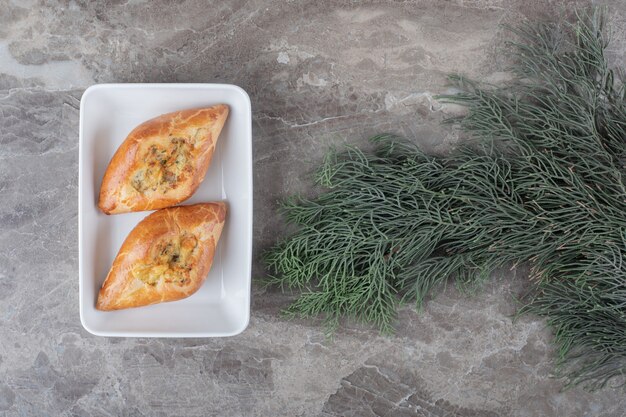 Dos pequeñas pides turcas en un plato junto a las ramas de pino en la superficie de mármol