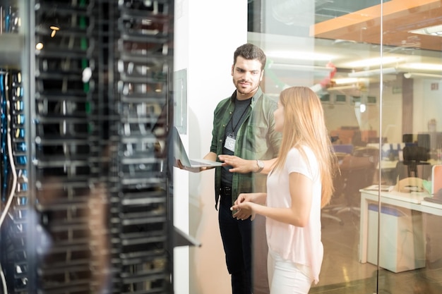 Dos personas de negocios de pie en la sala de servidores con una computadora portátil y discutiendo