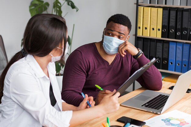 Dos personas en la oficina trabajando juntas durante la pandemia con máscaras médicas