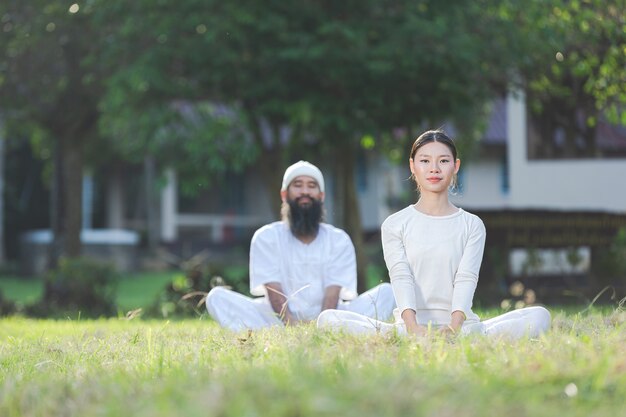 Dos personas en traje blanco haciendo yoga en la naturaleza