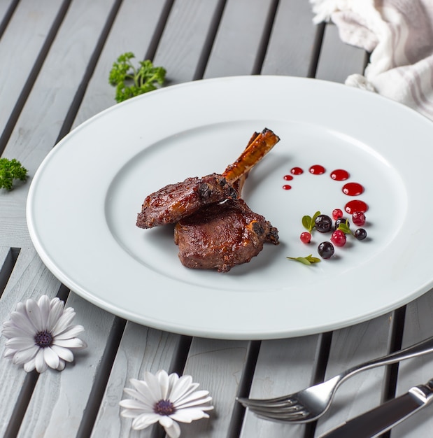 dos piezas de kebab de costillas de cordero en plato blanco adornado con salsa de bayas