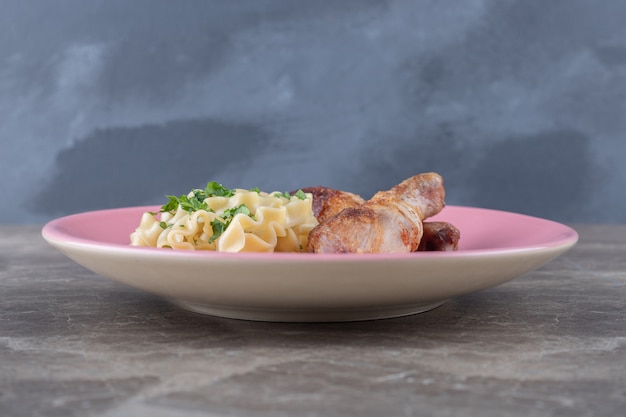 Dos piezas de muslo junto a la pasta en un plato, sobre la superficie de mármol.