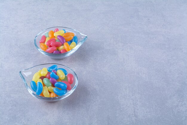 Dos placas de vidrio con caramelos de frijoles dulces de frutas sobre una superficie azul grisácea