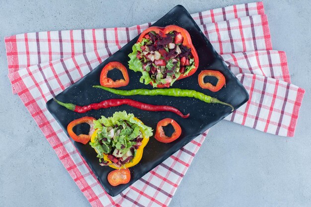 Dos porciones de ensalada en un plato decorado con rodajas de pimientos y chiles sobre la superficie de mármol