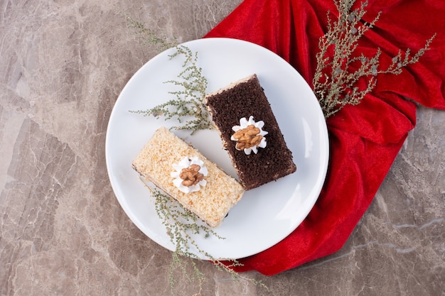 Dos rebanadas de pasteles en un plato blanco con mantel rojo.