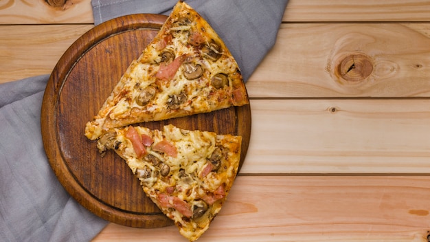 Dos rebanadas de pizza italiana de queso en bandeja de madera circular sobre la mesa
