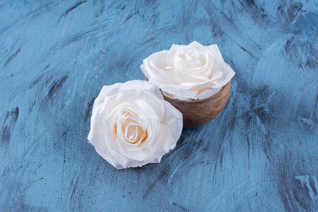 Foto gratuita dos rosas blancas en un tazón de madera en azul.