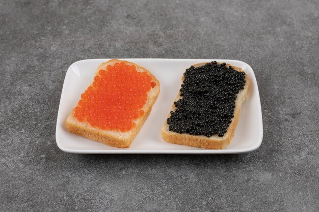 Dos sándwich con caviar rojo y negro sobre blanco y negro.