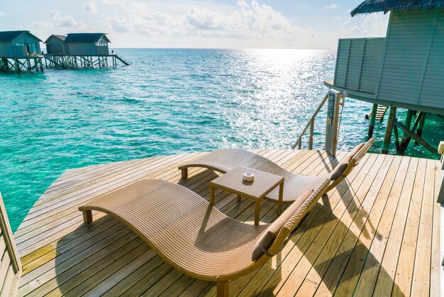 Dos sillas de cubierta en el piso de madera en el tiempo de la puesta del sol de la villa del agua, isla de maldives