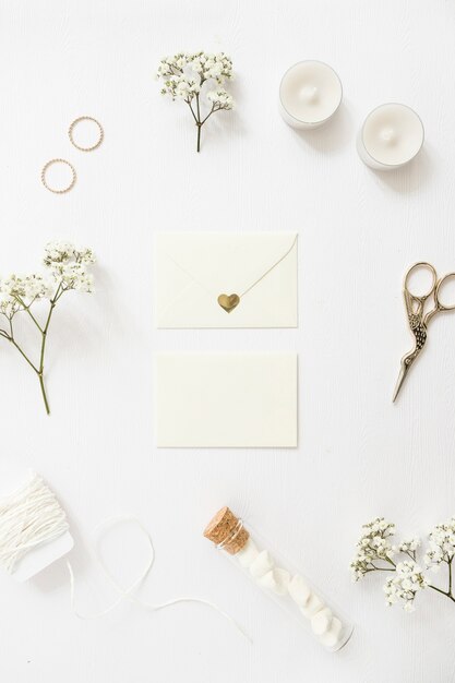 Dos sobres rodeados de anillos de boda; velas; cortar con tijeras; cuerda; Tubo de ensayo y flores de aliento de bebé sobre fondo blanco.