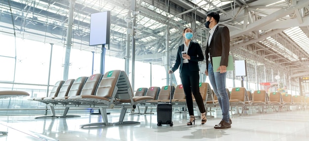 Dos socios comerciales asiáticos con protección de mascarilla facial distanciamiento social nuevo estilo de vida normal Viajeros de negocios caminando en el aeropuerto con equipaje