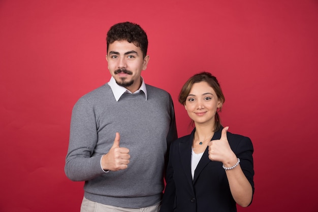 Foto gratuita dos socios comerciales dando pulgar hacia arriba en la pared roja