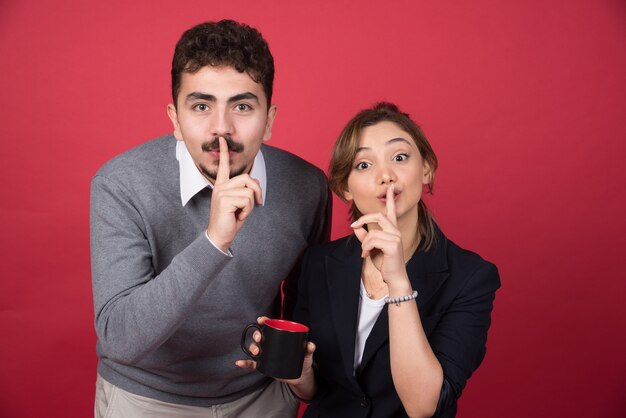 Dos socios comerciales dando señal de silencio en la pared roja