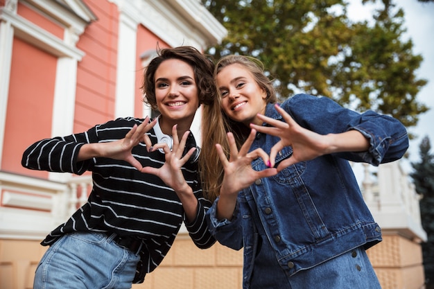 Foto gratuita dos sonrientes a adolescentes felices que muestran gesto de amor