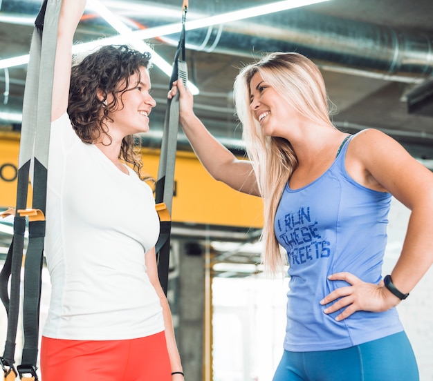 Dos sonrientes mujeres jóvenes atléticas mirando el uno al otro en el gimnasio