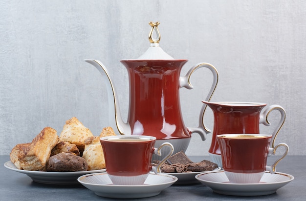 Dos tazas de café aromático con pasteles en mesa gris.