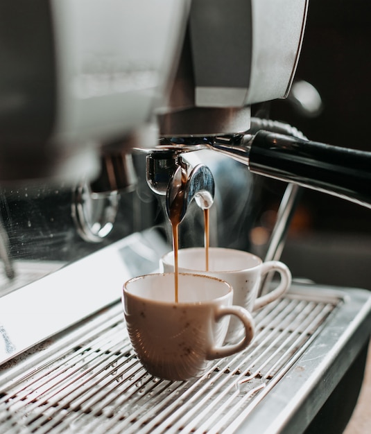 Dos tazas de café exprés debajo de la cafetera