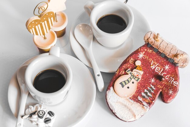 Dos tazas de café y guante de madera con texto de bienvenida y muñeco de nieve sobre fondo blanco