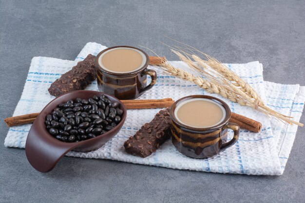 Dos tazas de café con hoja de papel y bombones sobre mantel.