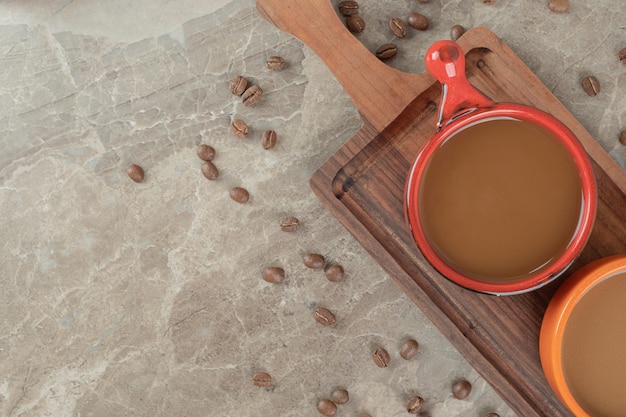 Dos tazas de café sobre tabla de madera con granos de café