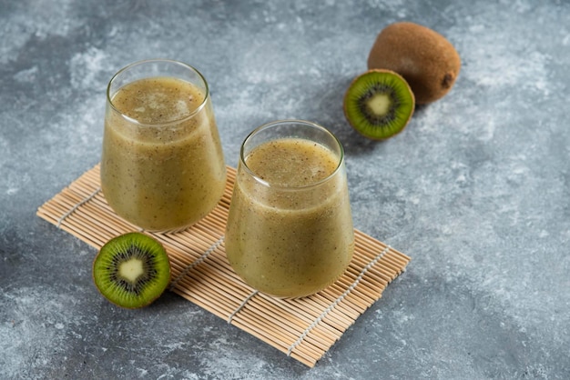 Dos tazas de cristal de delicioso jugo de kiwi en hoja de bambú.